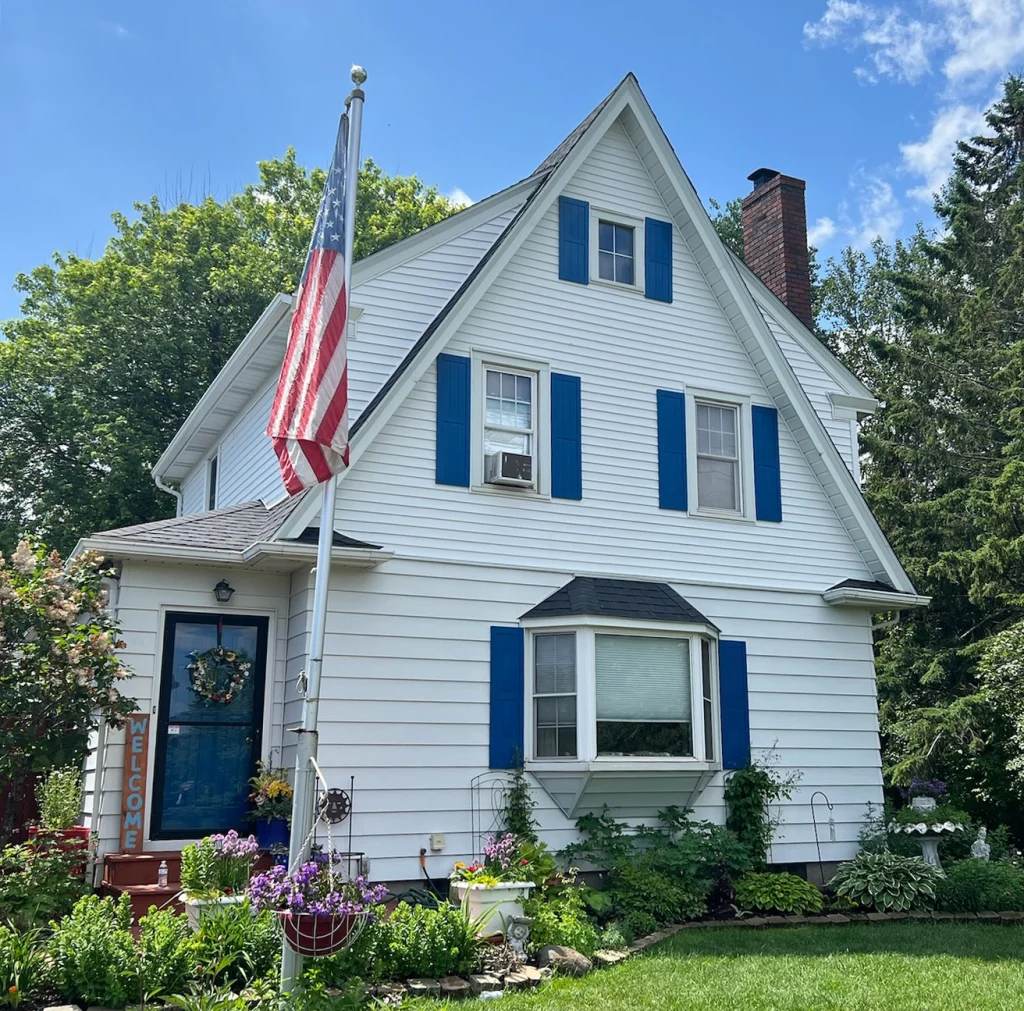 White house with blue shutters with an american flag in the yard